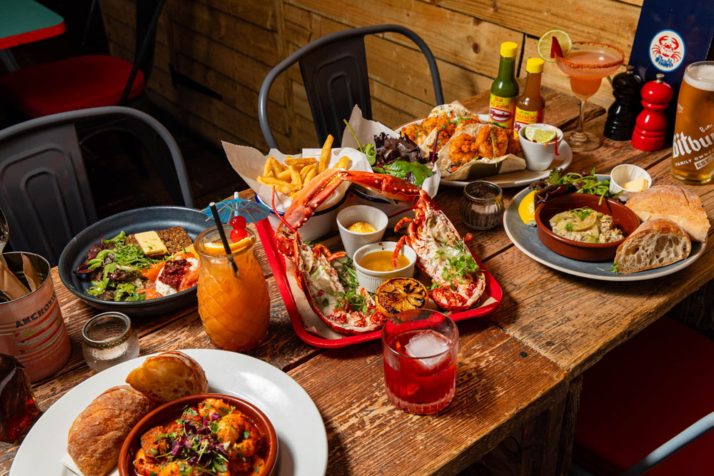 A table at Crabshack set with grilled lobster, prawns, cocktails and fresh bread on rustic wood
